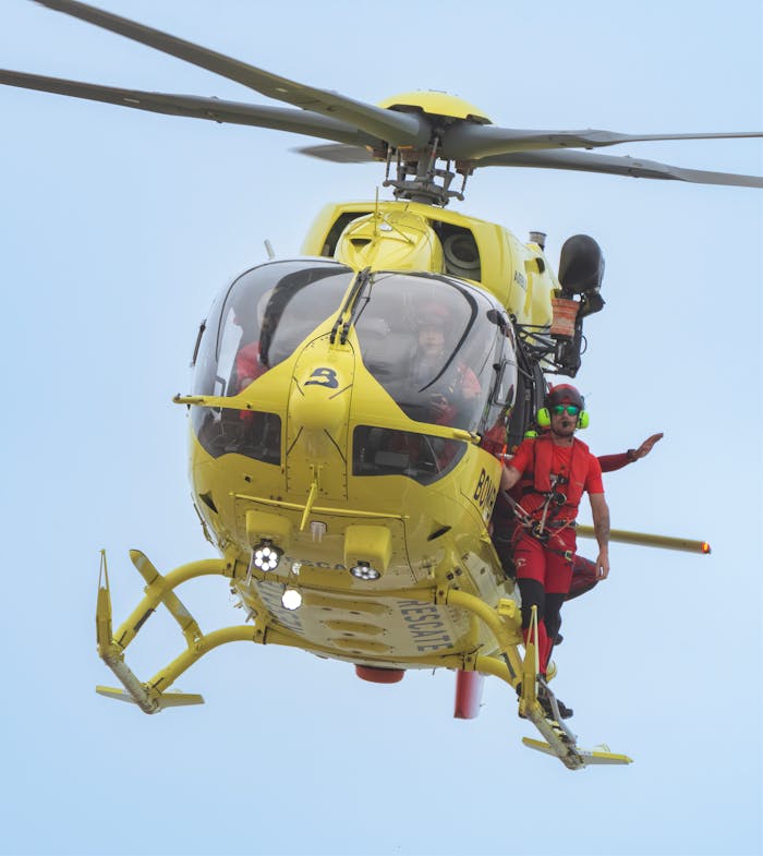 A yellow rescue helicopter in flight with a crew member leaning out, showcasing emergency response.