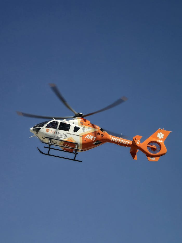 Orange and white medical helicopter flying against a clear blue sky.