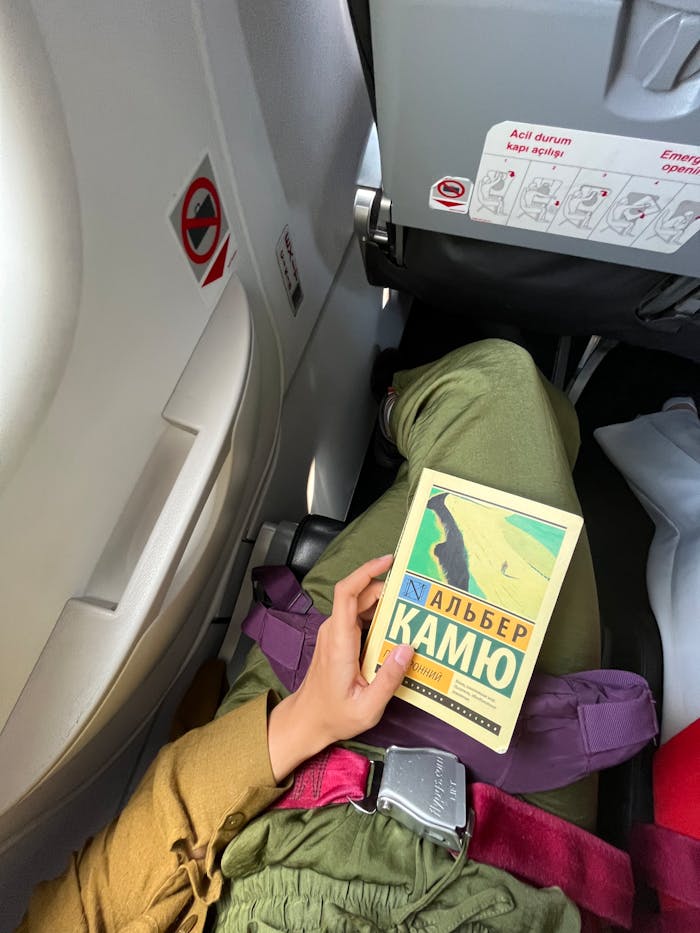 Passenger reading Albert Camus book on a flight. Captures travel and relaxation.