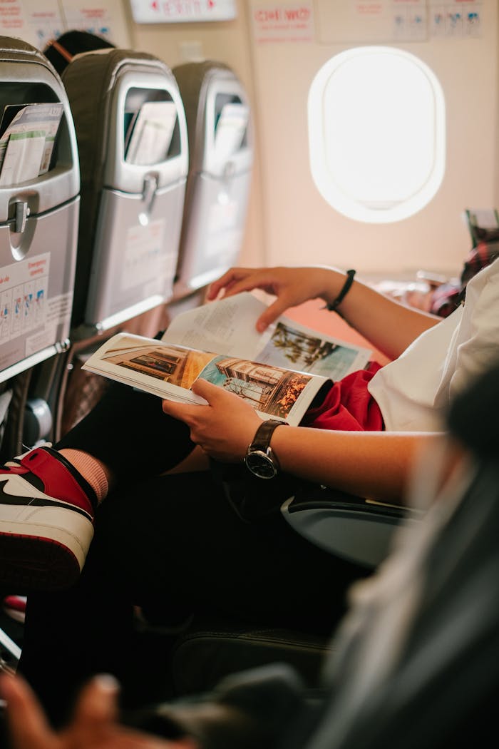Person reading a magazine while seated in an airplane, offering an in-flight experience.
