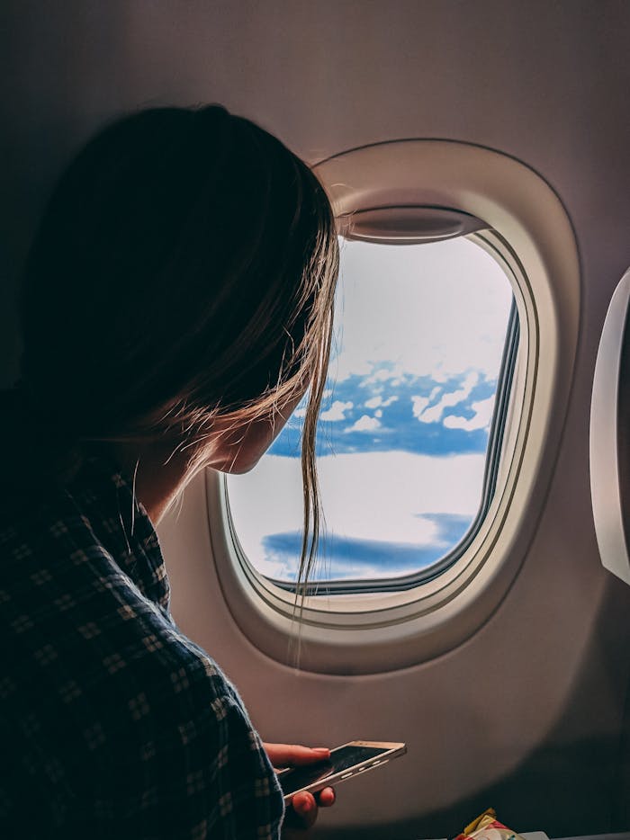 contact-img A woman looks out an airplane window, capturing a serene view of clouds and sky during a flight.