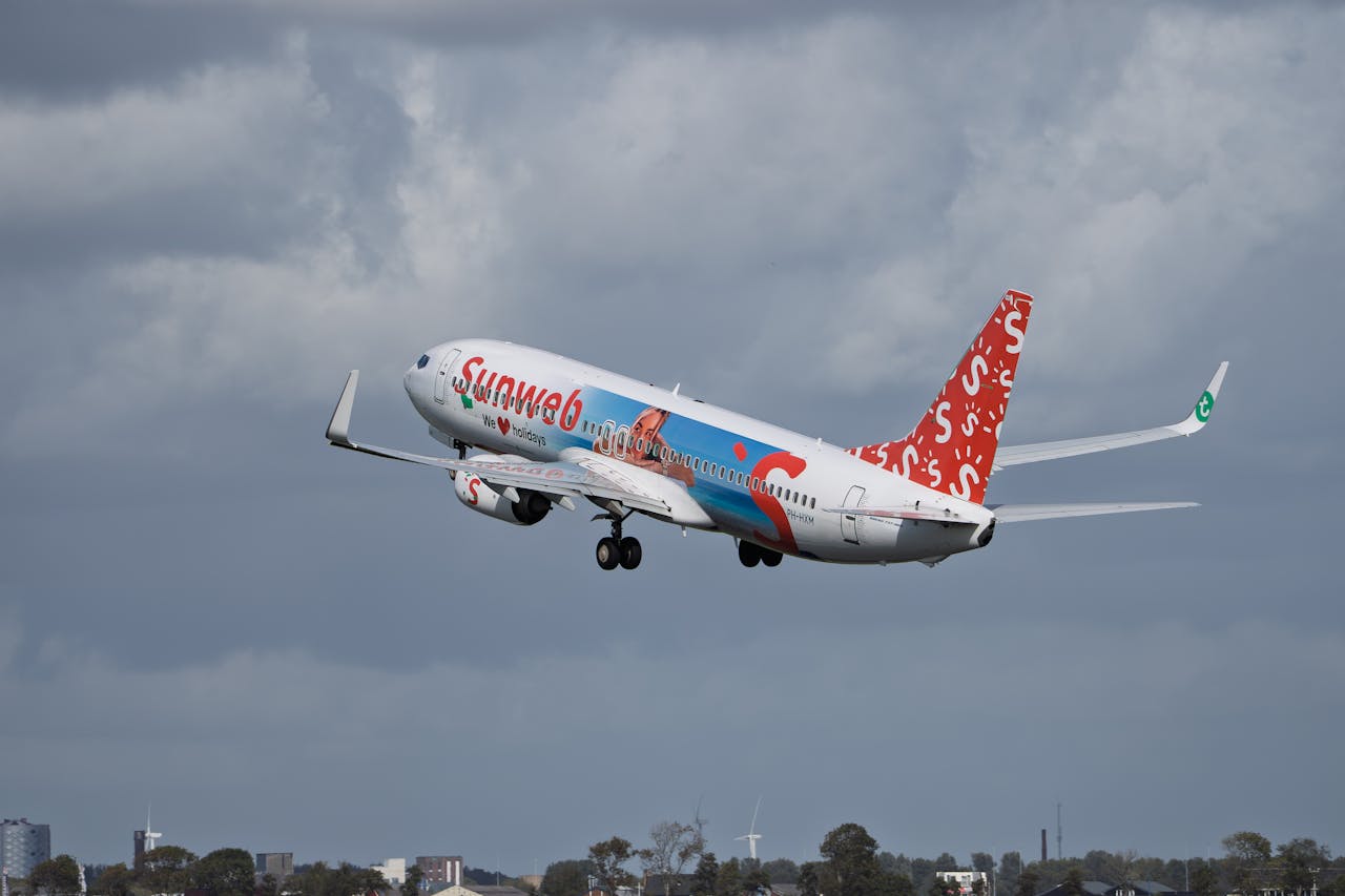 A commercial airplane with colorful branding takes off under a cloudy sky, symbolizing travel and adventure.